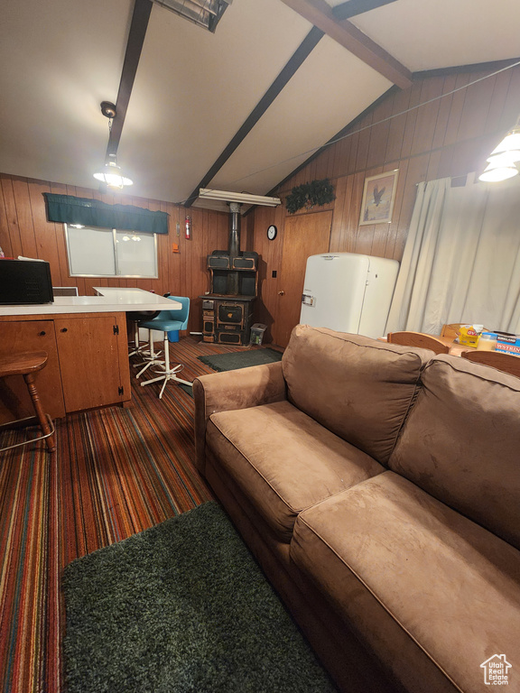 Living room featuring wooden walls, a wood stove, lofted ceiling, and dark carpet