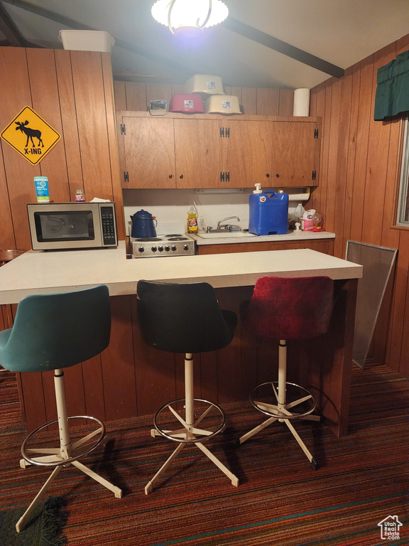 Kitchen featuring stainless steel microwave, light countertops, wood walls, a kitchen bar, and range