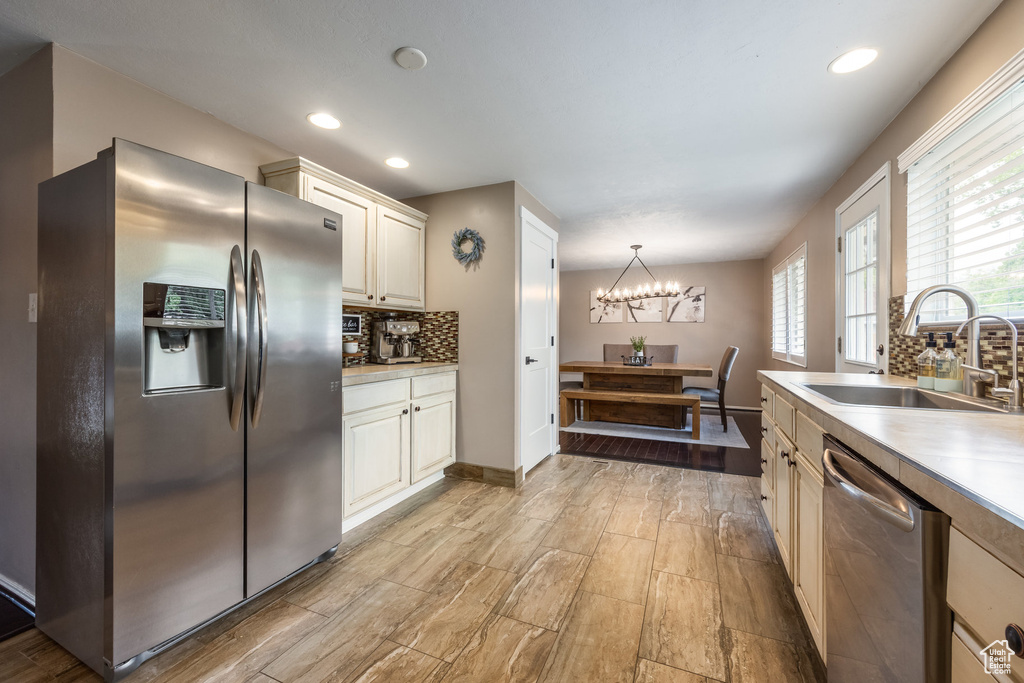 Kitchen featuring stainless steel appliances, a sink, a chandelier, decorative backsplash, and light countertops