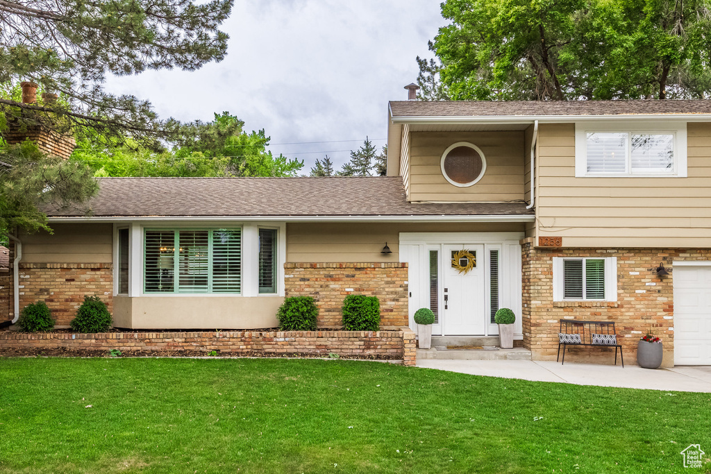 View of front of property featuring brick siding, a front yard, a garage, and roof with shingles