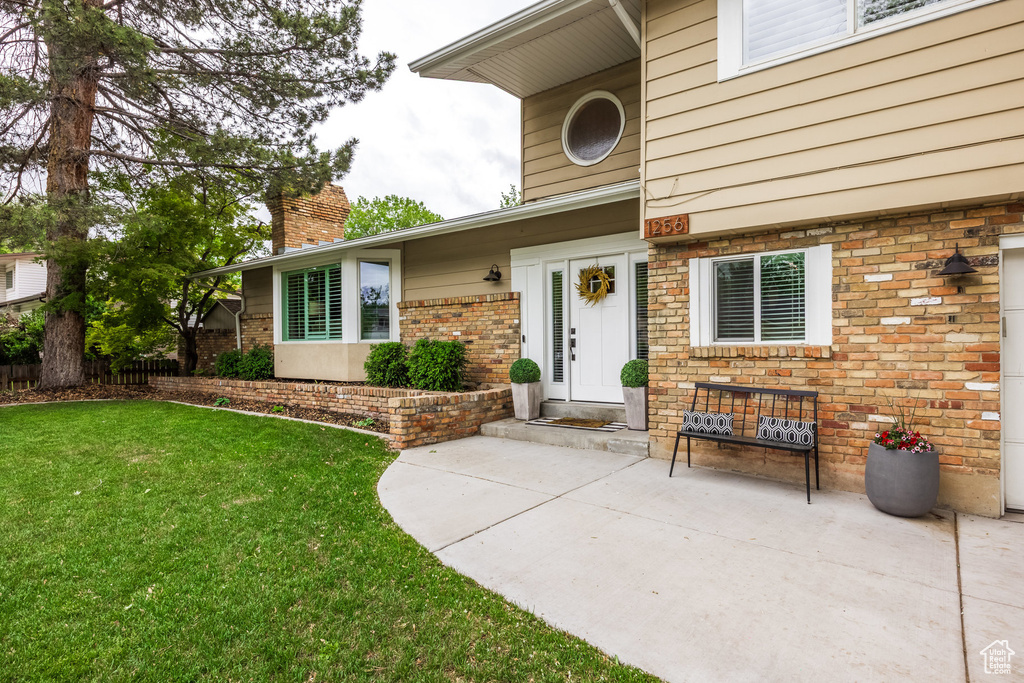 View of exterior entry with a yard, a chimney, and brick siding