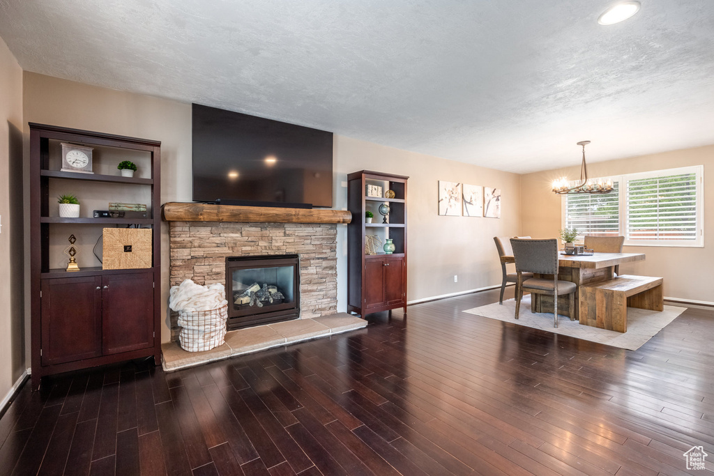 Living area featuring baseboards, wood finished floors, a chandelier, a fireplace, and a textured ceiling