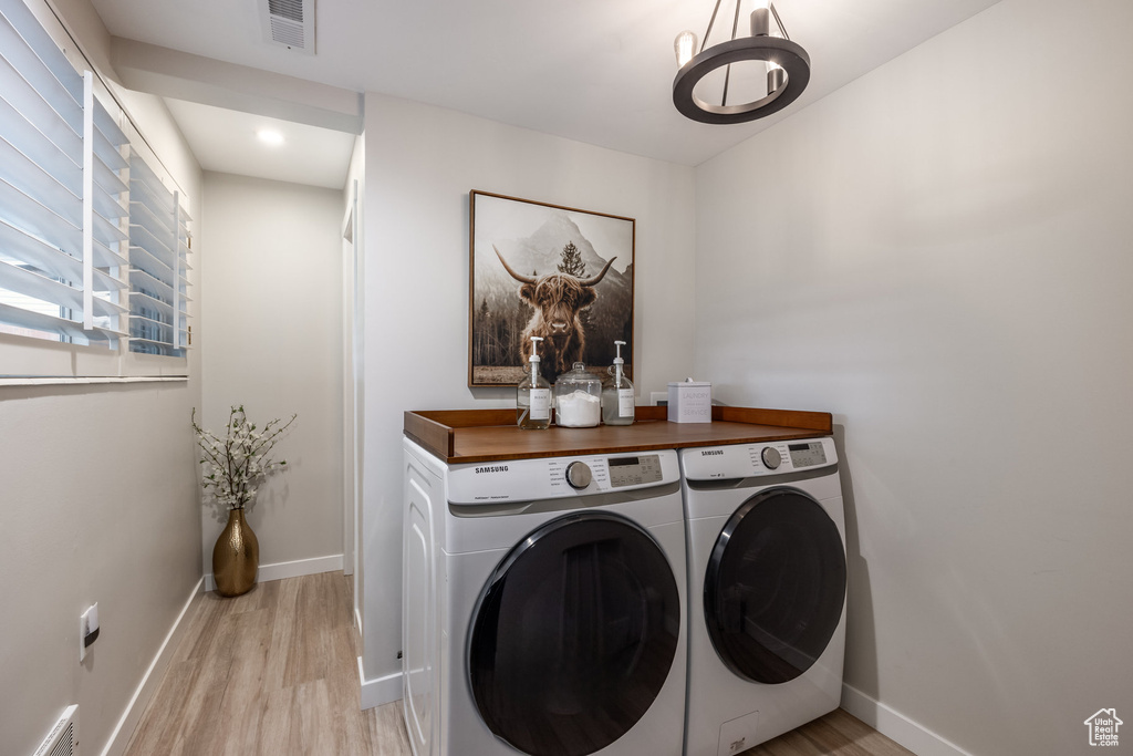 Clothes washing area with washing machine and dryer, light wood-type flooring, baseboards, a chandelier, and recessed lighting