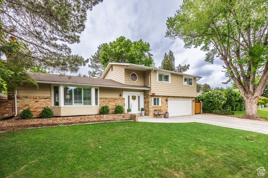 Split level home featuring brick siding, driveway, an attached garage, and a front lawn