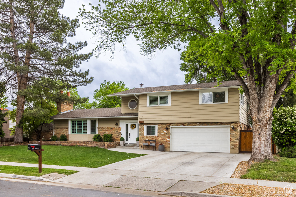 Tri-level home featuring a garage, concrete driveway, brick siding, and a chimney