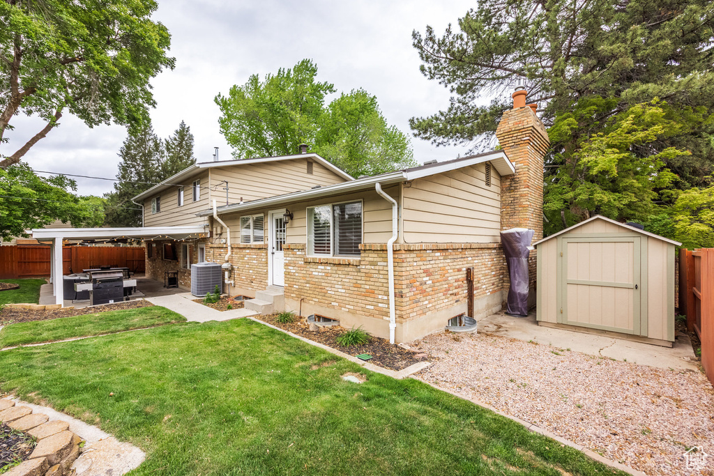 Back of property with brick siding, a hot tub, a patio area, a storage unit, and a chimney