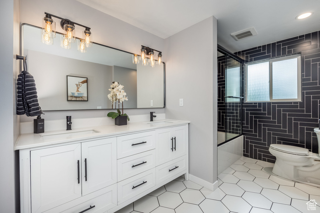 Full bathroom with toilet, tile patterned floors, double vanity, bath / shower combo with glass door, and recessed lighting