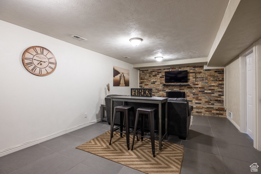 Bar area featuring a textured ceiling, tile patterned flooring, baseboards, brick wall, and a brick fireplace
