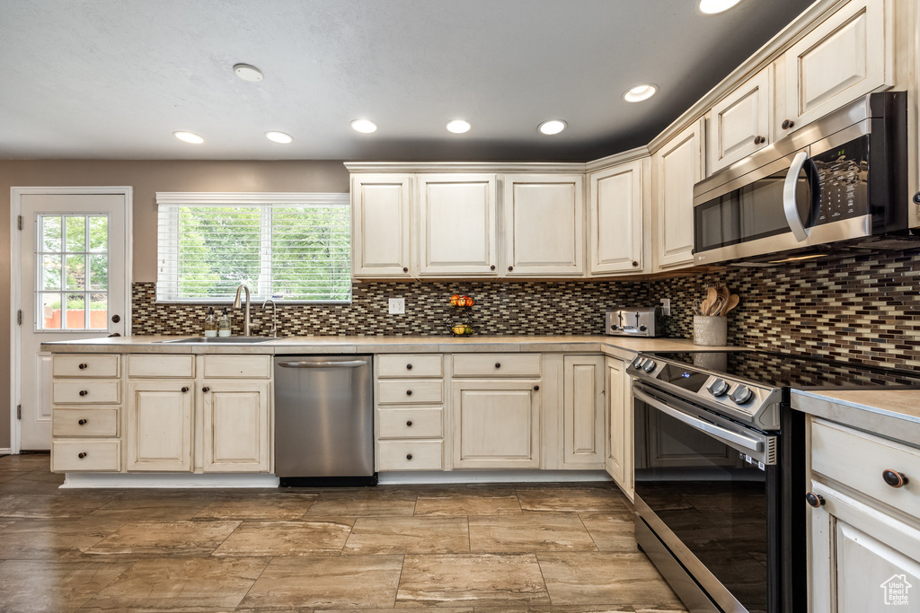Kitchen featuring appliances with stainless steel finishes, a sink, recessed lighting, backsplash, and light countertops
