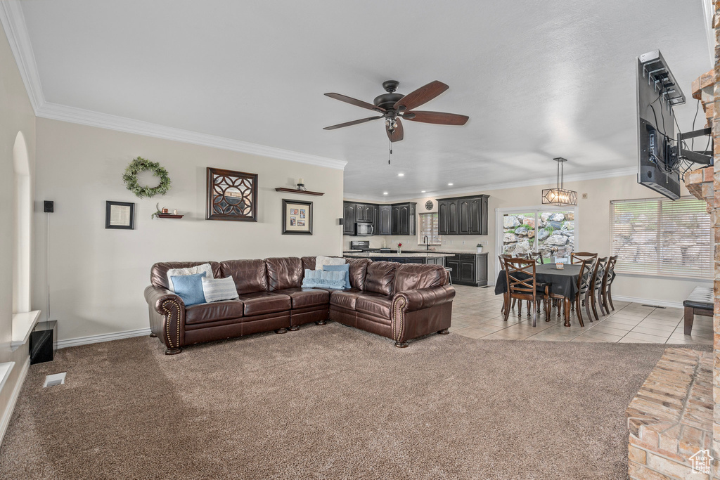 Living room featuring ceiling fan, crown molding, baseboards, arched walkways, and light colored carpet