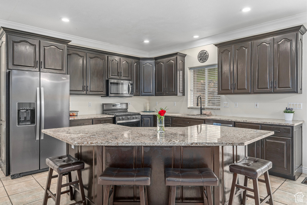 Kitchen with appliances with stainless steel finishes, a sink, light tile patterned floors, a breakfast bar, and ornamental molding