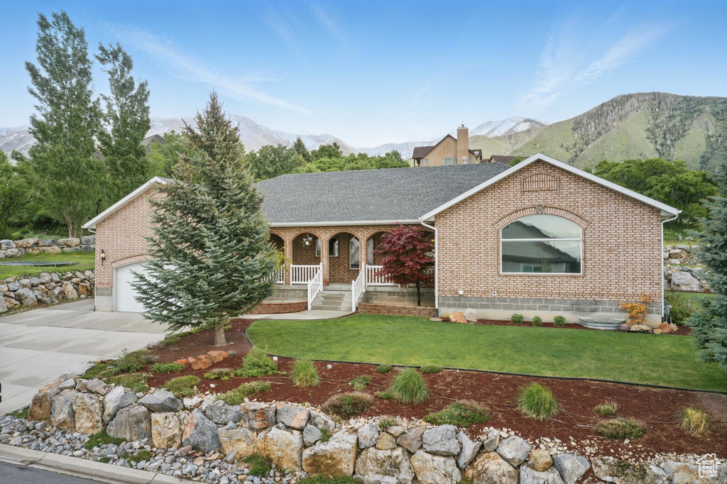 View of front of property featuring brick siding, a mountain view, a porch, concrete driveway, and a front yard