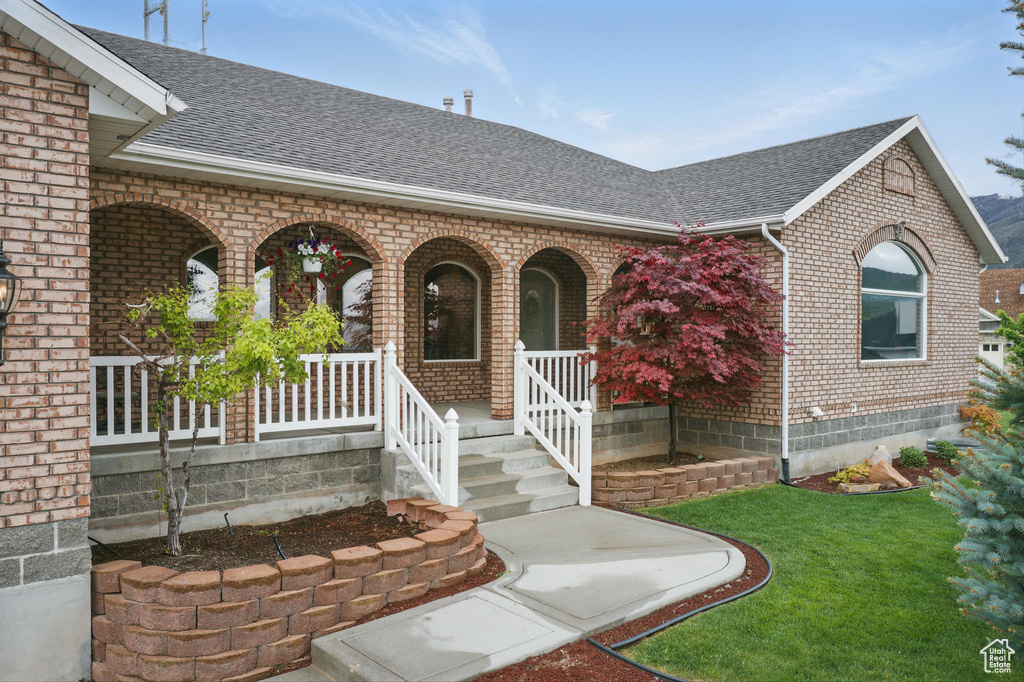 Doorway to property with brick siding, roof with shingles, covered porch, and a yard