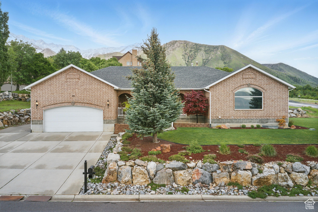 Single story home featuring brick siding, driveway, a mountain view, a front lawn, and an attached garage