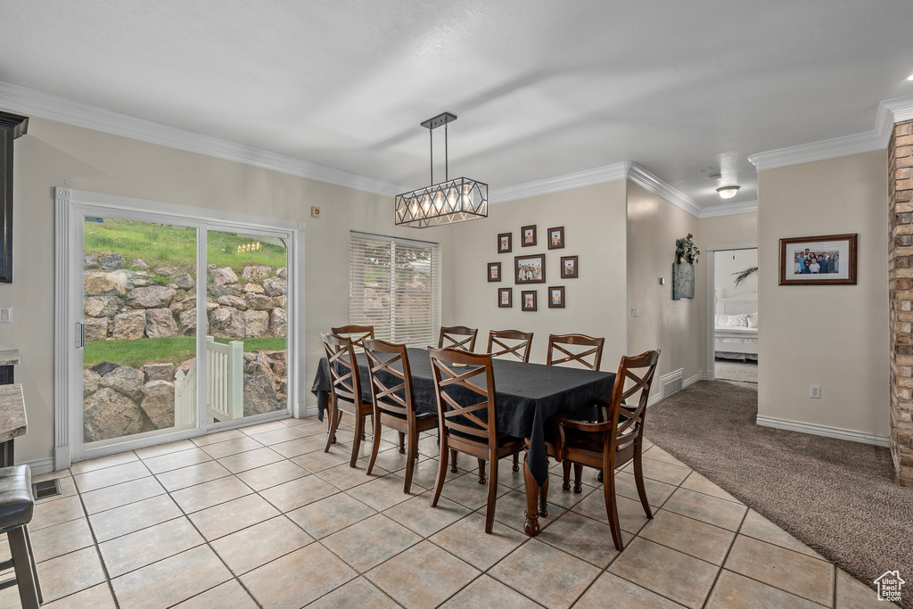 Dining space with light tile patterned floors, a chandelier, crown molding, light carpet, and baseboards