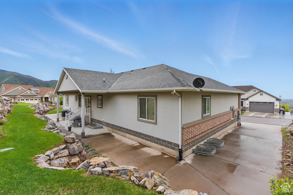 Back of house with a yard, a patio area, roof with shingles, a mountain view, and an outbuilding