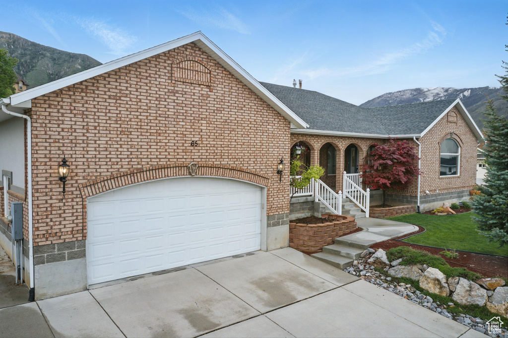 View of front of home with brick siding, concrete driveway, a mountain view, and covered porch