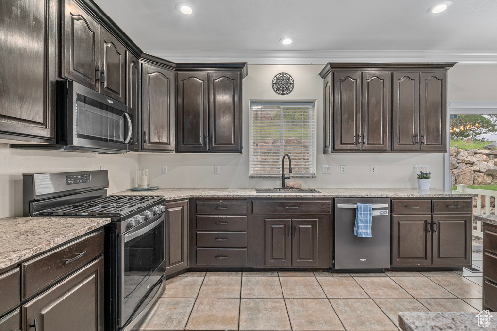 Kitchen featuring stainless steel appliances, a sink, light tile patterned flooring, ornamental molding, and dark brown cabinets