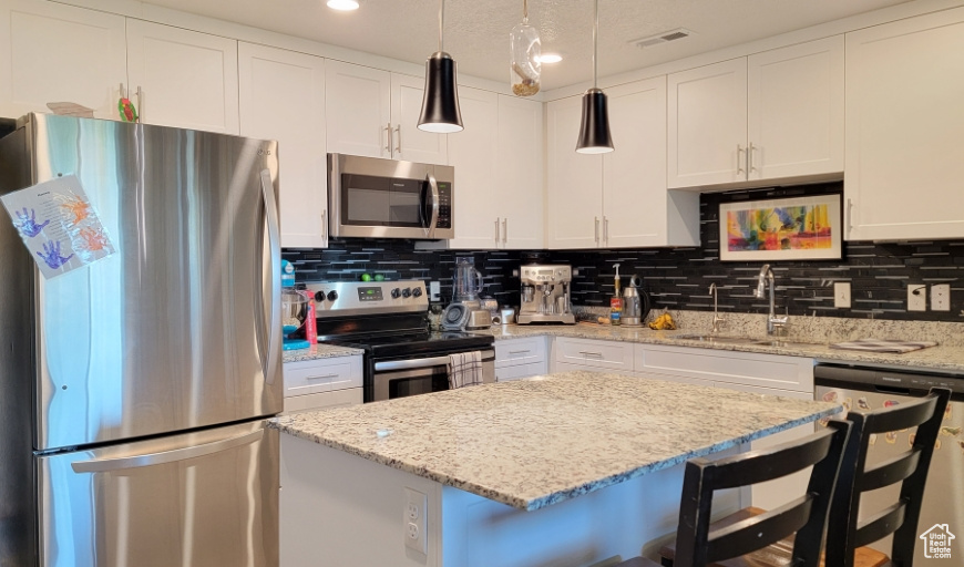 Kitchen with stainless steel appliances, a sink, a kitchen breakfast bar, white cabinets, and backsplash