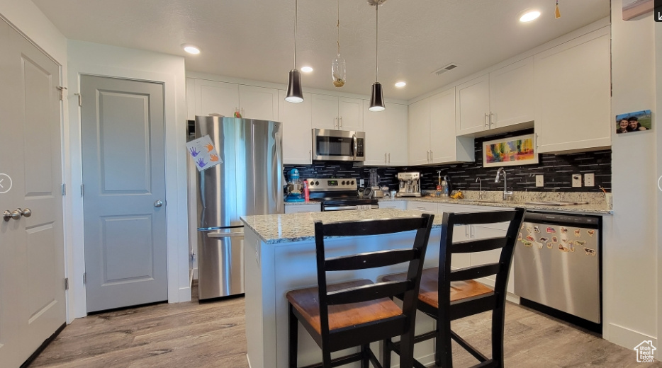 Kitchen featuring appliances with stainless steel finishes, light wood-style flooring, tasteful backsplash, white cabinets, and a center island