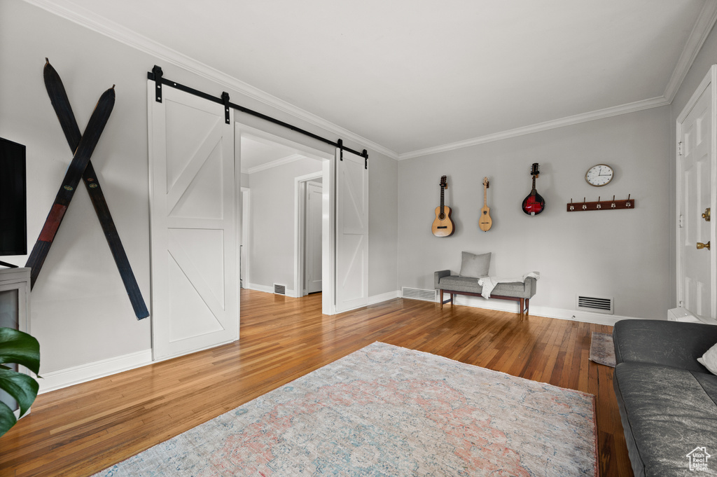 Living room with a barn door, wood finished floors, ornamental molding, and baseboards