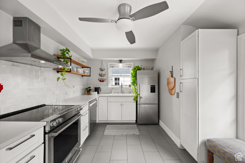 Kitchen featuring stainless steel appliances, wall chimney range hood, a sink, light tile patterned floors, and white cabinets