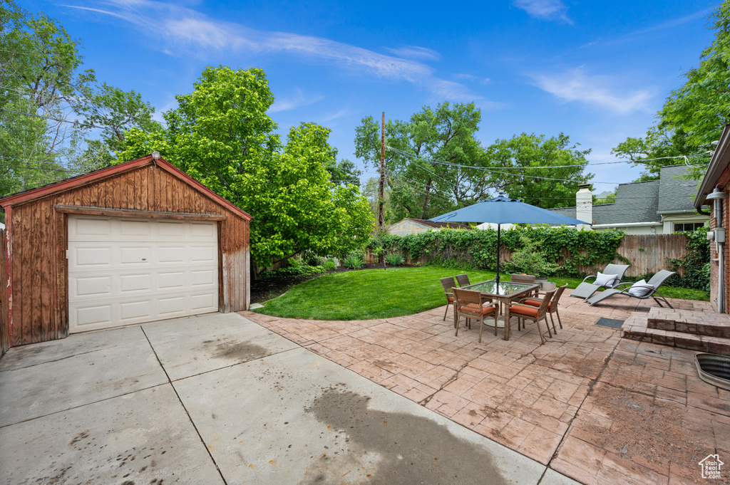 View of patio featuring driveway, a garage, an outdoor structure, and outdoor dining area