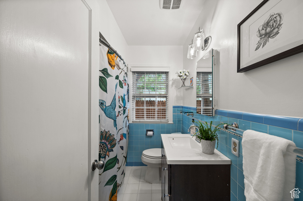 Full bathroom with vanity, toilet, tile walls, tile patterned floors, and a wainscoted wall