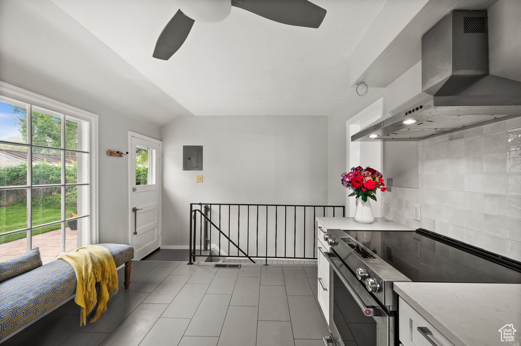 Kitchen featuring stainless steel electric range oven, wall chimney exhaust hood, a ceiling fan, white cabinets, and light tile patterned flooring