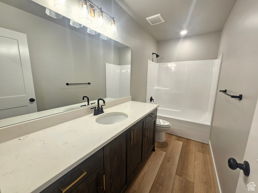 Bathroom with wood finished floors, vanity, tub / shower combination, and toilet