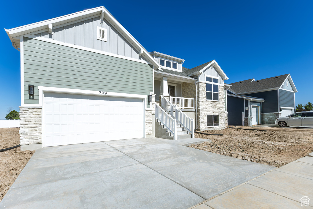 Craftsman-style home featuring stone siding, board and batten siding, driveway, and covered porch