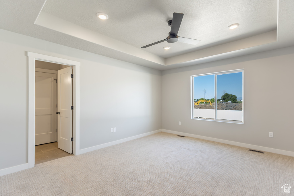 Empty room featuring a raised ceiling, light colored carpet, a ceiling fan, and recessed lighting