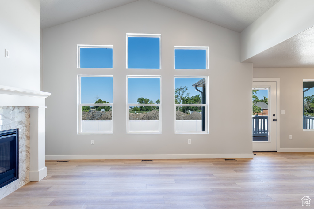 Unfurnished living room featuring a fireplace, light wood finished floors, and high vaulted ceiling