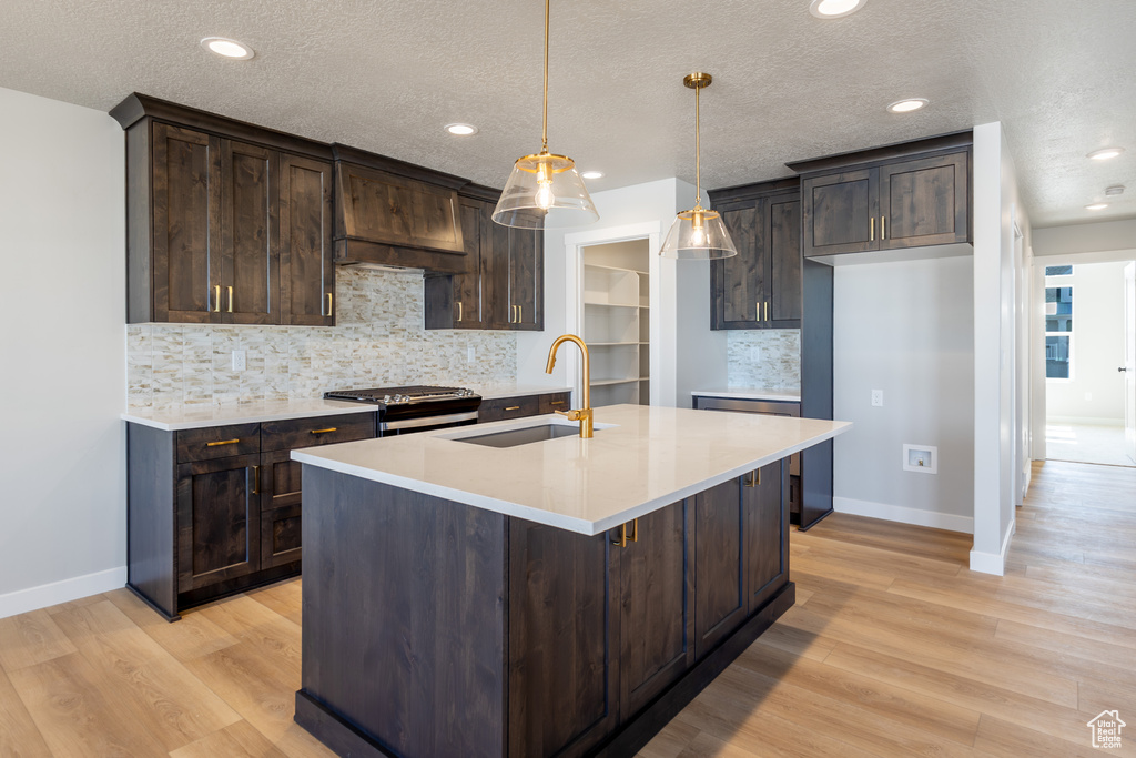 Kitchen with range with gas stovetop, dark brown cabinets, light wood finished floors, recessed lighting, and a textured ceiling