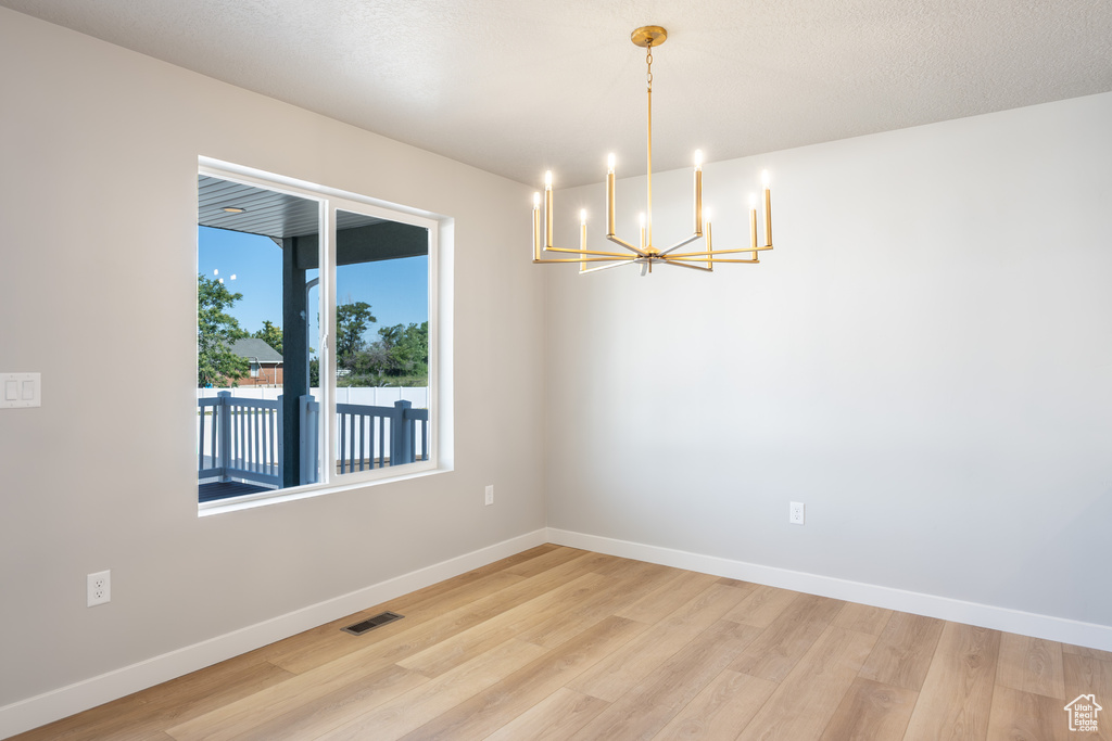 Unfurnished room featuring a chandelier and light wood-style flooring