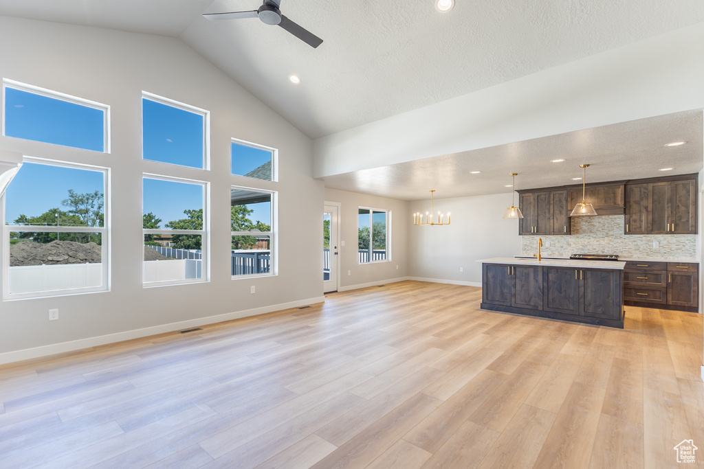 Unfurnished living room with a chandelier, a ceiling fan, high vaulted ceiling, light wood finished floors, and recessed lighting