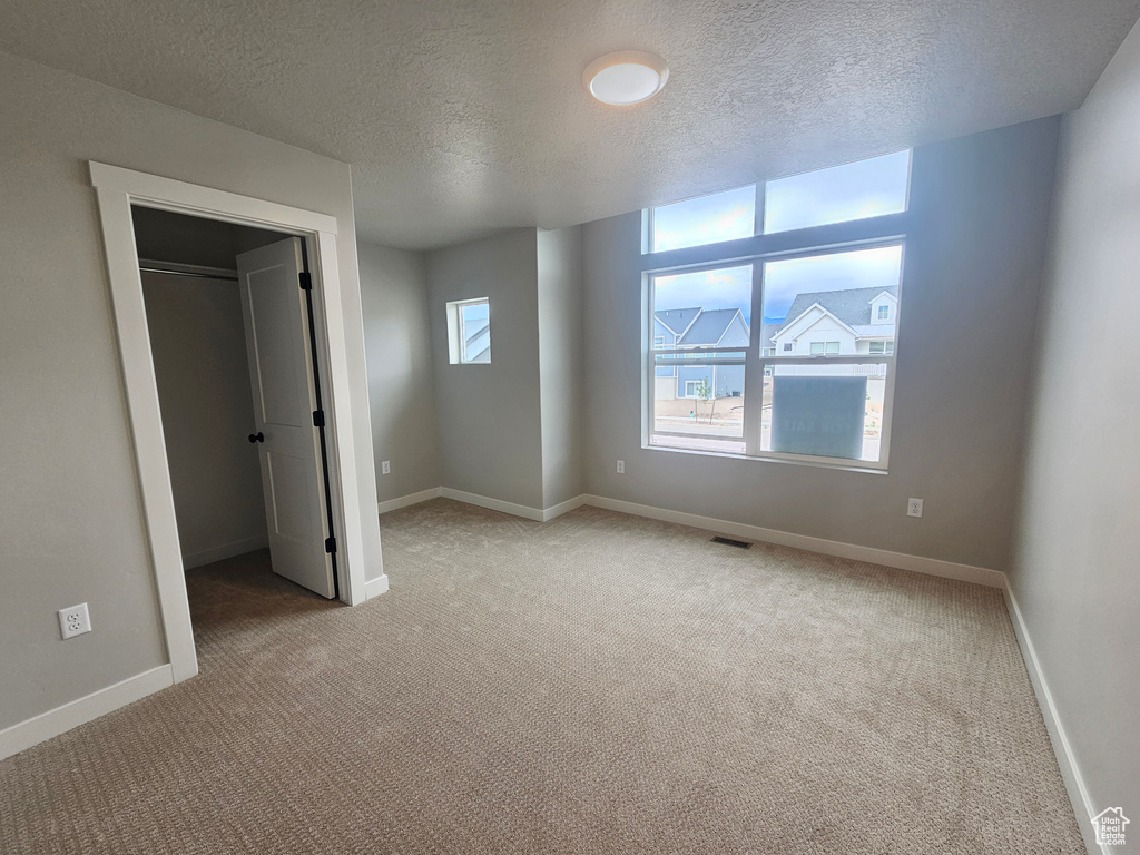 Unfurnished bedroom featuring light colored carpet, a textured ceiling, baseboards, and a spacious closet
