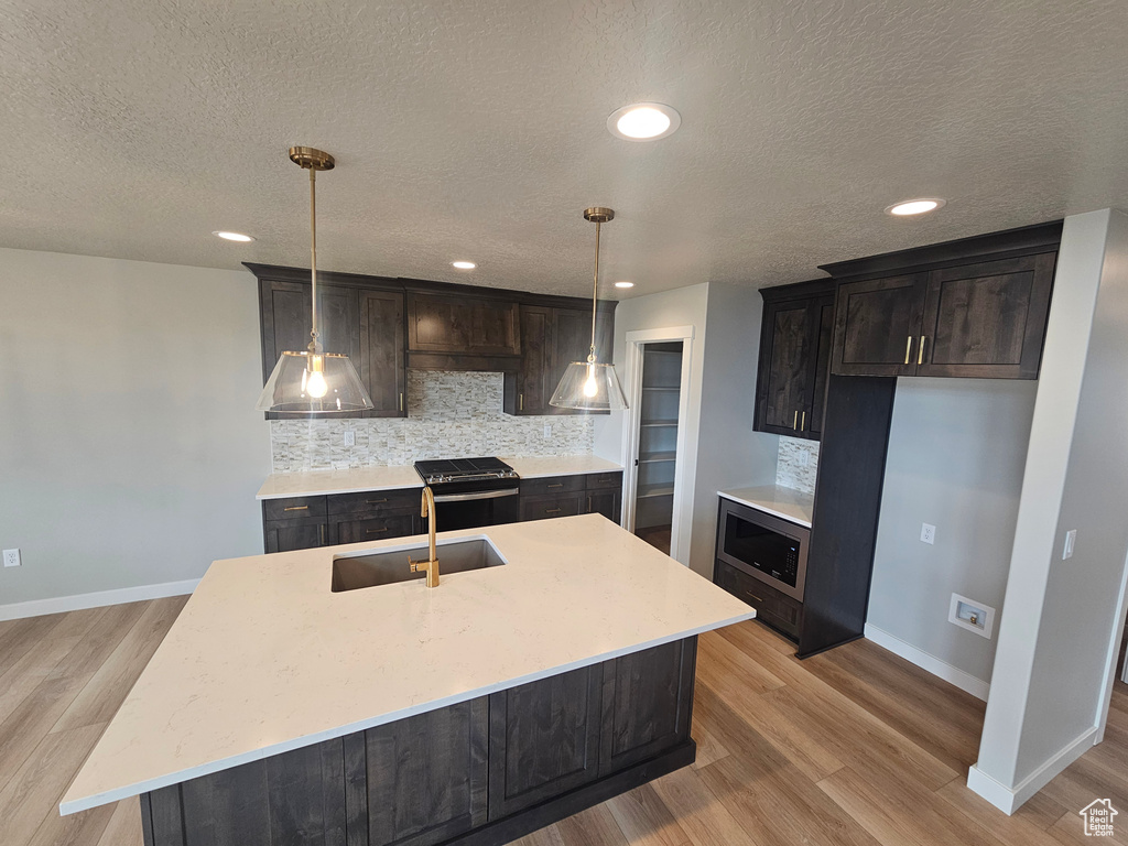 Kitchen featuring stainless steel microwave, tasteful backsplash, a sink, baseboards, and light wood finished floors
