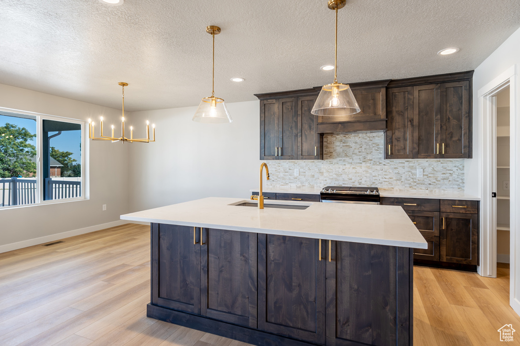 Kitchen with black electric range oven, backsplash, light wood-type flooring, dark brown cabinetry, and a textured ceiling