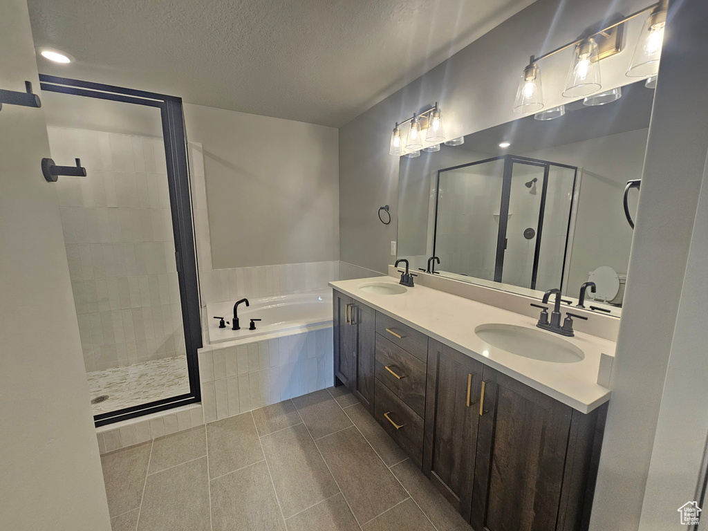 Full bathroom featuring a shower stall, a garden tub, double vanity, a textured ceiling, and tile patterned floors
