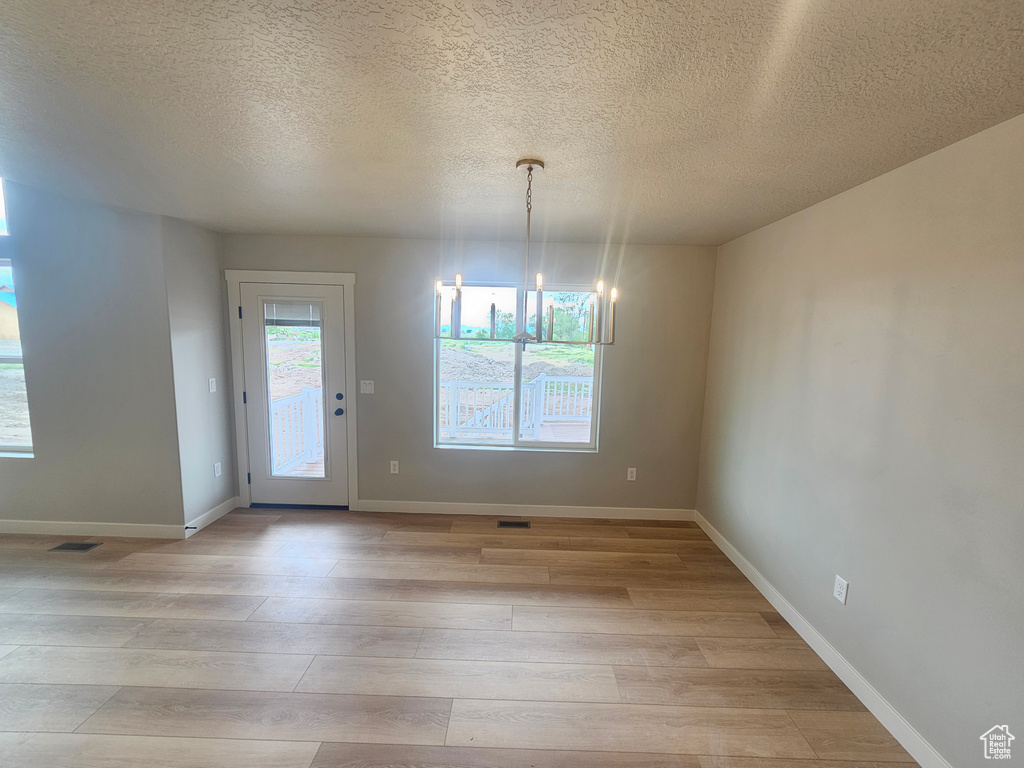 Unfurnished dining area featuring light wood-style floors, a chandelier, a textured ceiling, and baseboards