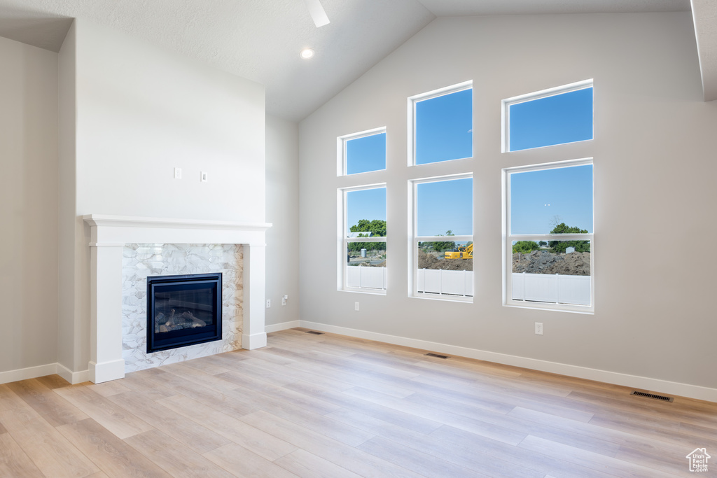 Unfurnished living room featuring high vaulted ceiling, a high end fireplace, and light wood-style floors