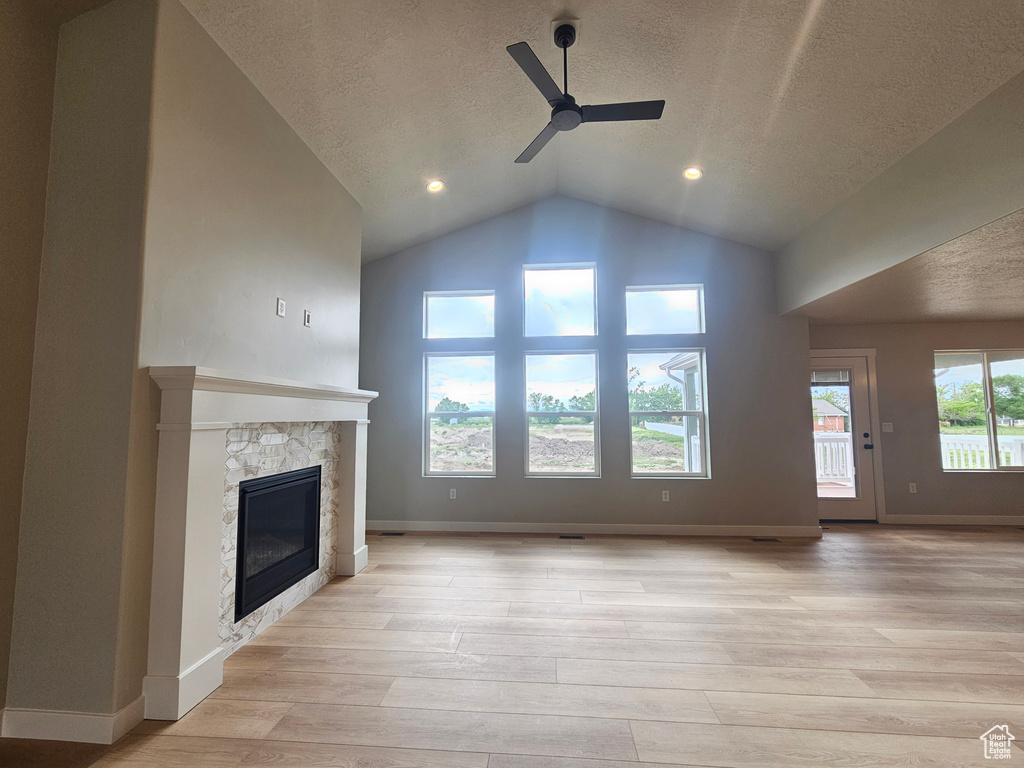 Unfurnished living room with ceiling fan, light wood-style flooring, a textured ceiling, a glass covered fireplace, and vaulted ceiling