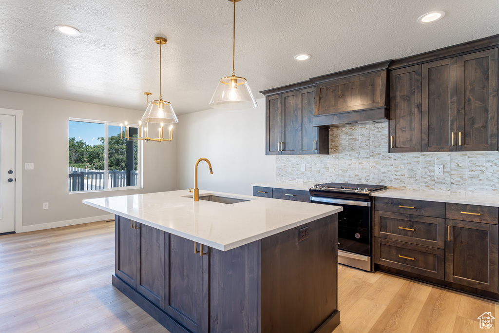 Kitchen with stainless steel stove, light wood-type flooring, tasteful backsplash, light countertops, and a textured ceiling