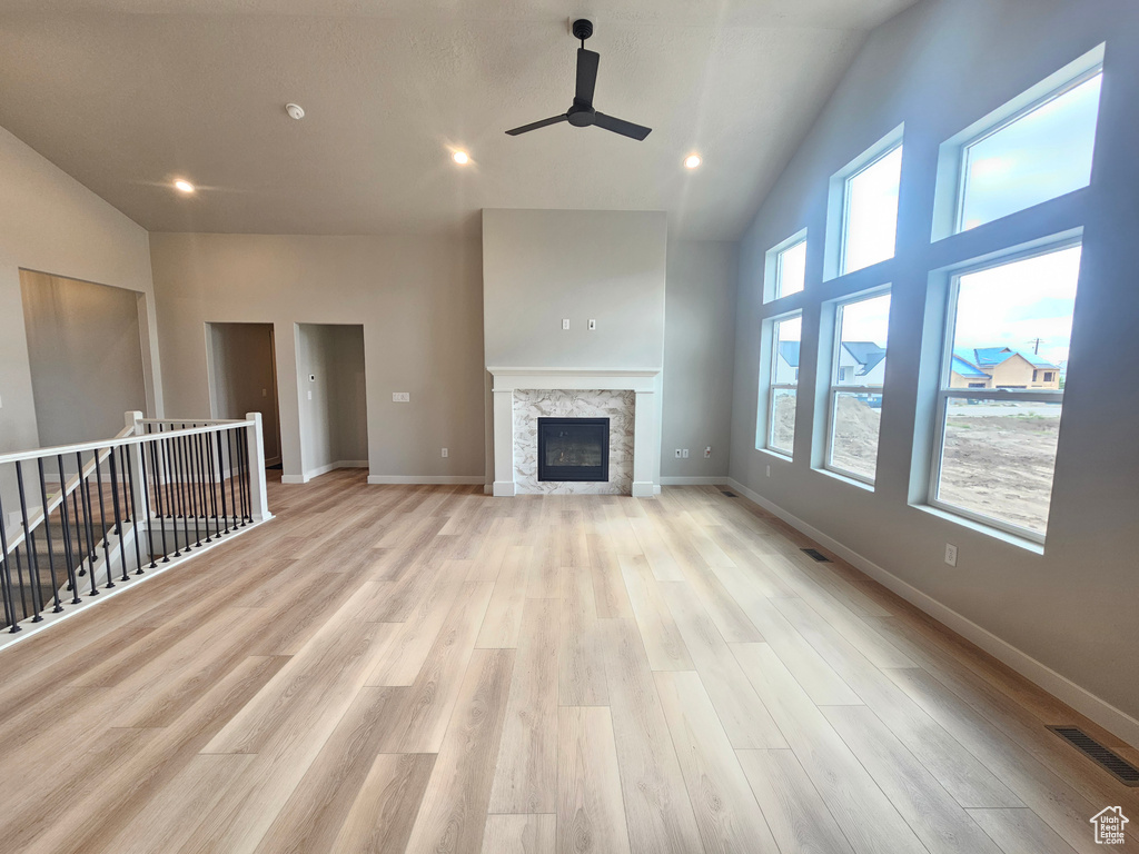 Unfurnished living room with ceiling fan, light wood-style flooring, baseboards, high vaulted ceiling, and a tiled fireplace