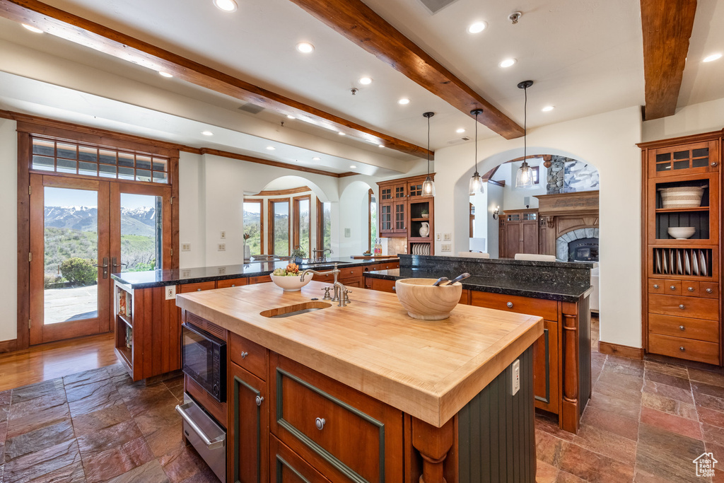 Kitchen featuring a large island, beamed ceiling, stone tile flooring, built in microwave, and french doors
