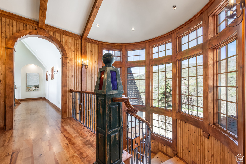Corridor featuring arched walkways, an upstairs landing, wood-type flooring, wood walls, and beam ceiling