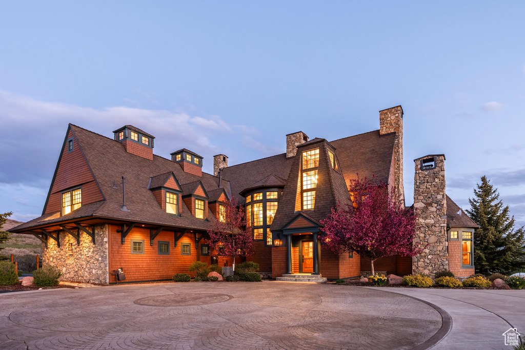 Shingle-style home with curved driveway, a chimney, a shingled roof, and stone siding