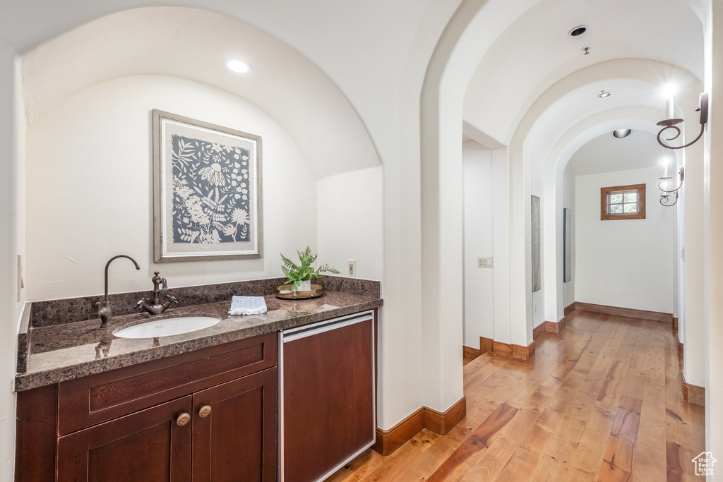 Bar with a sink, light wood-style floors, arched walkways, and baseboards