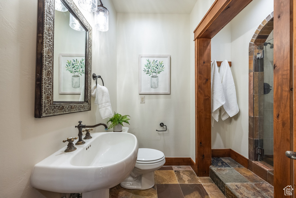Full bathroom featuring stone tile floors, a stall shower, toilet, a sink, and baseboards